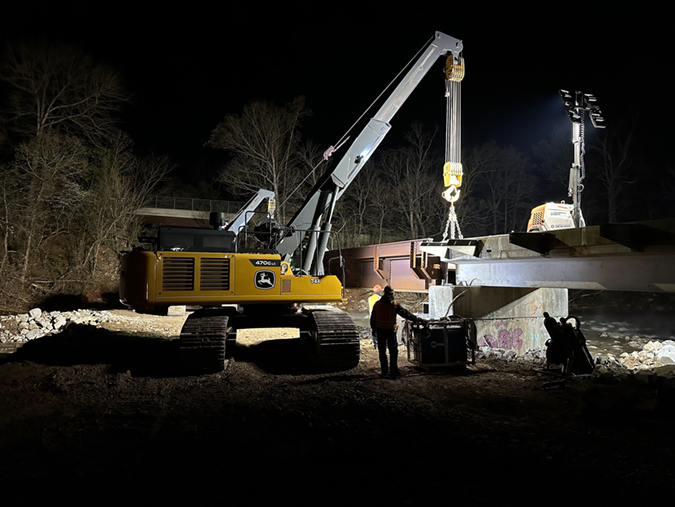 Bridge assembly continues at 4:00 a.m. on April 9. The first train over the completed bridge is shown in photo at top.