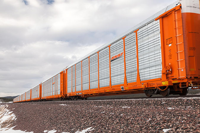 Auto rack train rolls through plains with mountain range in distance.